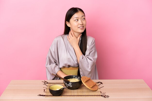 Niña china vistiendo kimono y comiendo fideos mirando hacia arriba mientras sonríe