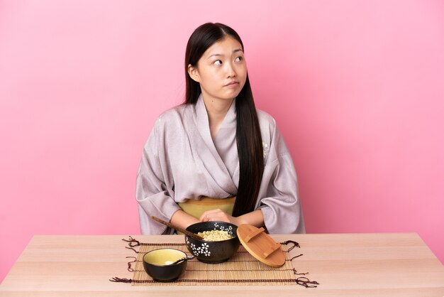 Niña china vistiendo kimono y comiendo fideos y mirando hacia arriba