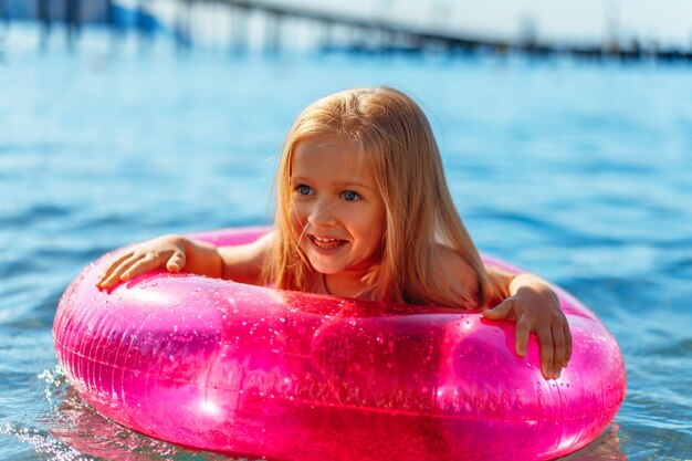 Niña con círculo inflable rosa bañándose en el mar