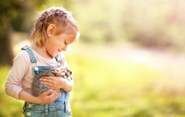 Una niña en un claro soleado sostiene un conejo en sus brazos y sonríe.