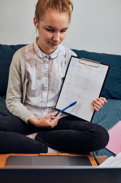 Niña con clipboard llamando por video mientras está sentada en casa