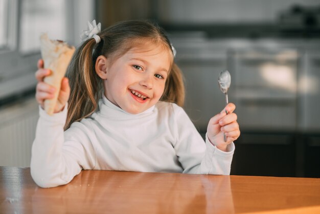 La niña en la cocina comiendo el helado con una cuchara la luz del día muy dulce