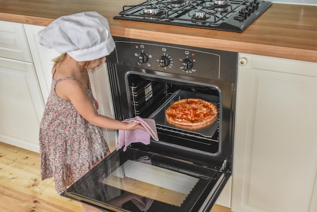 La niña cocina pizza en la foto del horno sin filtro.