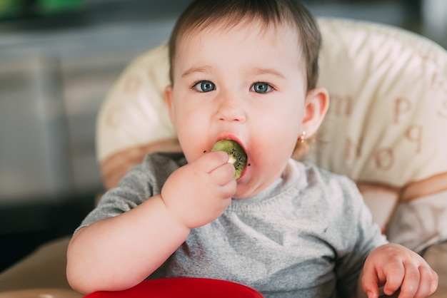 Niña en la cocina en una silla alta comiendo kiwi