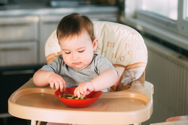 niña en la cocina en una silla alta comiendo kiwi