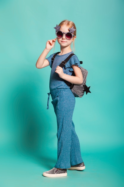 Niña con una cola en ropa elegante y gafas de sol sobre fondo azul