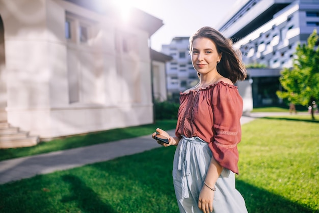 Foto niña colegiala sosteniendo un teléfono en sus manos mirando la cámara al aire libre