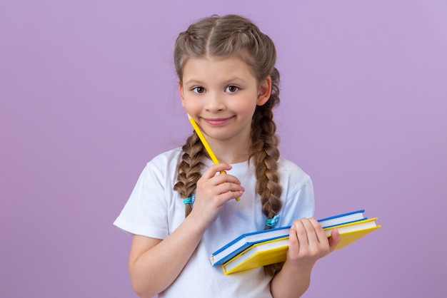 Una niña con coletas en una camiseta blanca y libros en sus manos sobre un fondo púrpura aislado.