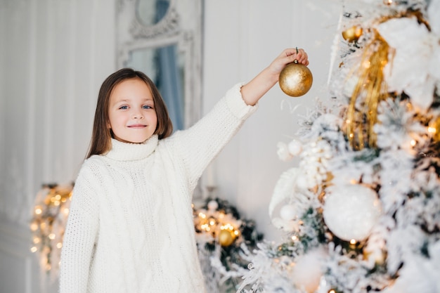 Niña colgando adorno en árbol de Navidad