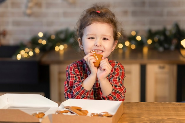 Foto niña come galletas de navidad de hombre de jengibre caseras tradicionales en año nuevo