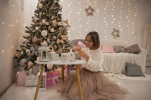 Niña come mandarina junto al árbol de Navidad