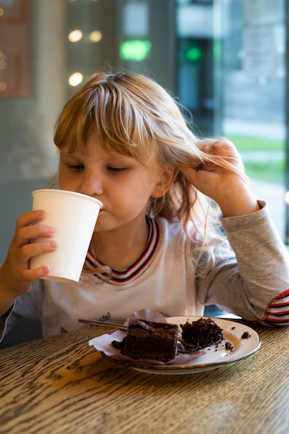 niña come pastel de chocolate de postre en un café