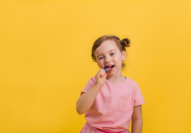 Una niña come una piruleta en un palo en un amarillo aislado