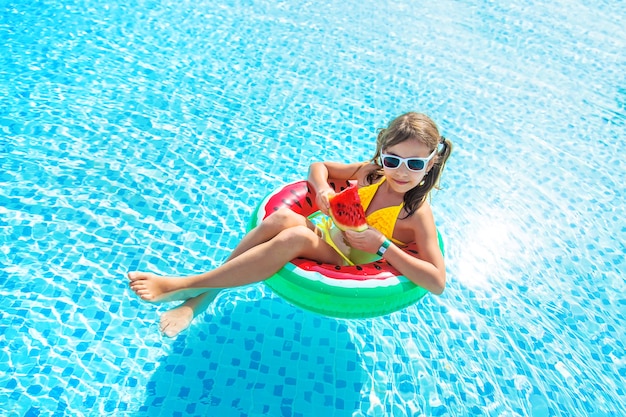 Niña come sandía en una sandía inflable en la piscina