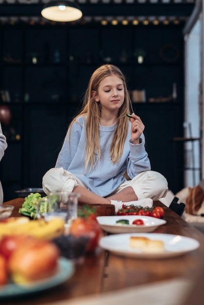 Niña come verduras sentado en la mesa de la cocina.