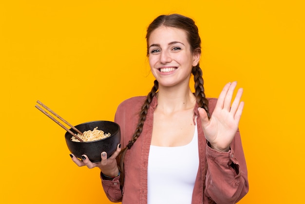 Niña comiendo fideos sobre pared amarilla aislada