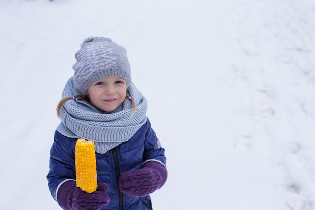 Niña comiendo maíz al aire libre en días de invierno