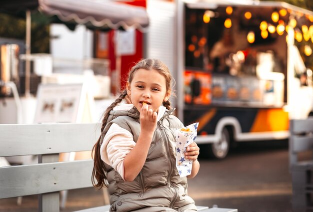 Foto niña comiendo papas fritas con salsa en el café de la calle afuera. concepto de comida rápida y niños.