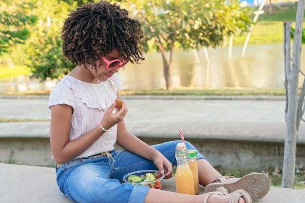 Niña comiendo verduras mientras se sienta en el parque en verano