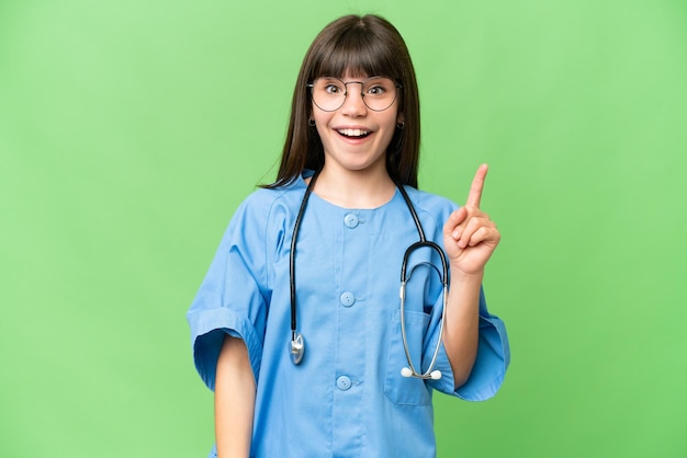 Niña como médico cirujano sobre un fondo aislado de clave de croma señalando con el dedo índice una gran idea