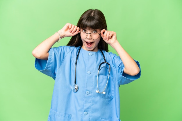 Niña como médico cirujano sobre fondo clave de croma aislado con gafas y sorprendido