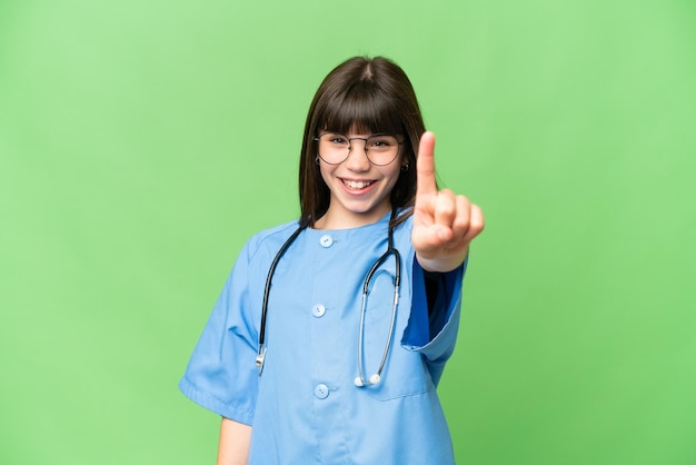 Niña como médico cirujano sobre un fondo de clave de croma aislado que muestra y levanta un dedo