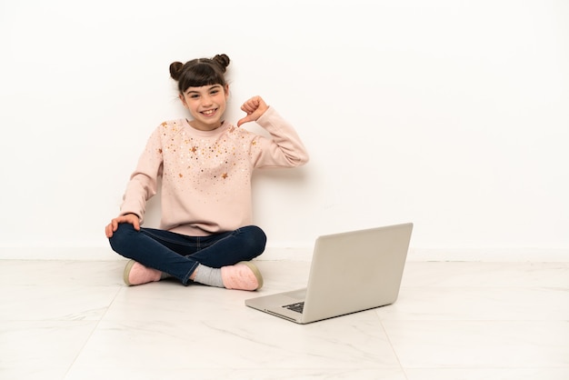 Niña con una computadora portátil sentada en el suelo orgullosa y satisfecha de sí misma