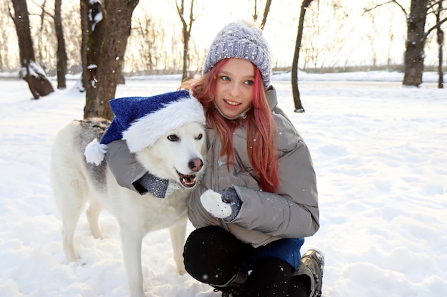 La niña se comunica felizmente con el perro con el sombrero de Santa Claus en la naturaleza en invierno.