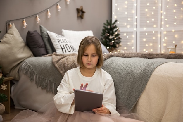 La niña se comunica en la tableta, felicitaciones por el Año Nuevo y Navidad de forma remota.