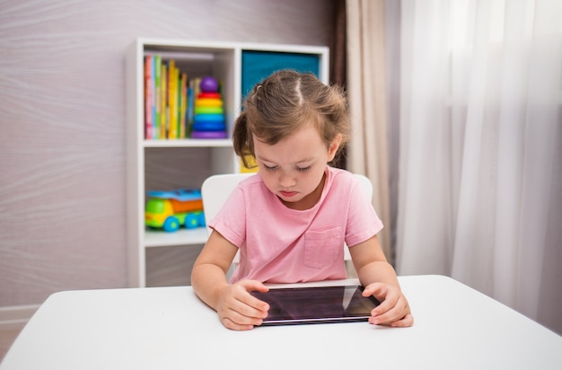 Niña concentrada jugando con una tableta en una mesa en la habitación