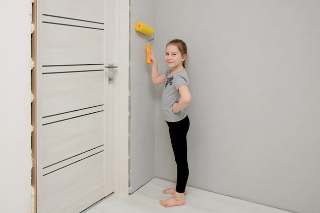 La niña conduce a lo largo de la pared con un rodillo de pintura en una casa que está siendo renovada