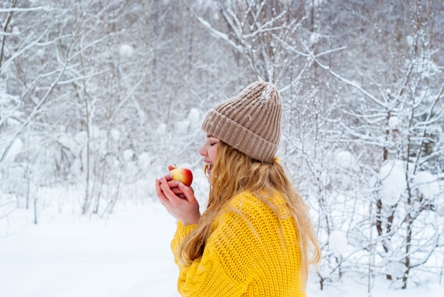 Niña congelada contra el paisaje invernal quiere morder un trozo de manzana