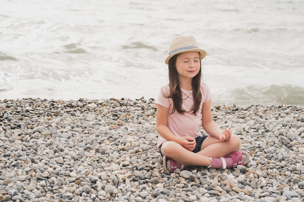 Una niña consciente medita en la orilla del mar una niña hace yoga maduración psicológica ...