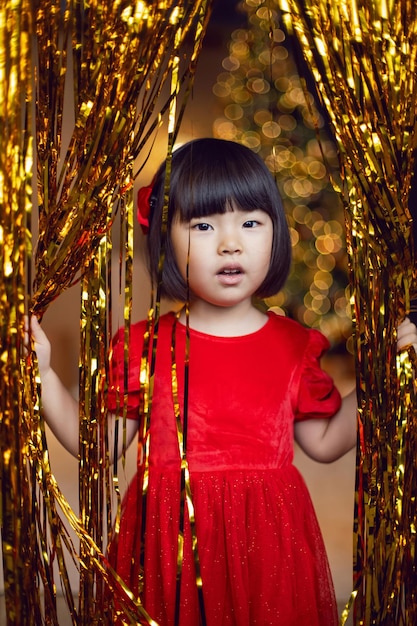 Niña coreana en vestido rojo está jugando en la noche de Navidad con oropel dorado