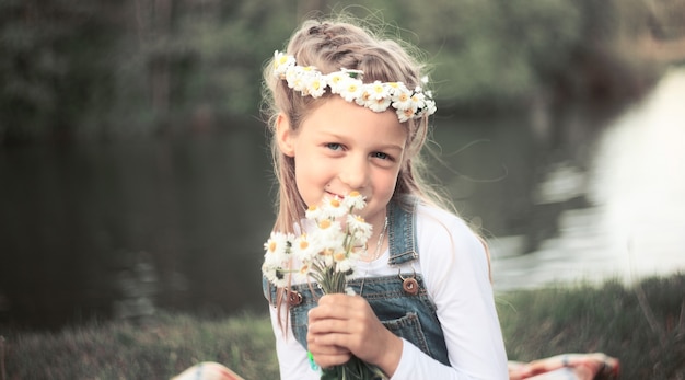 Niña en una corona de margaritas y un ramo de flores en el parque en un día soleado