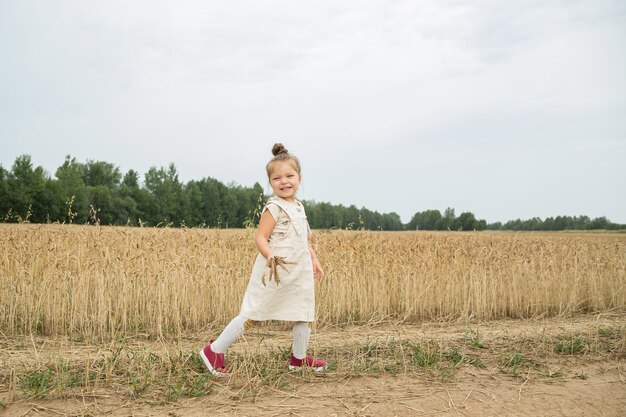 una niña corre por un campo de trigo con espiguillas en las manos y se ríe