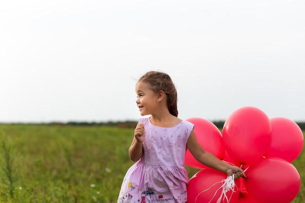 niña corre con globos rojos en el verano en la naturaleza