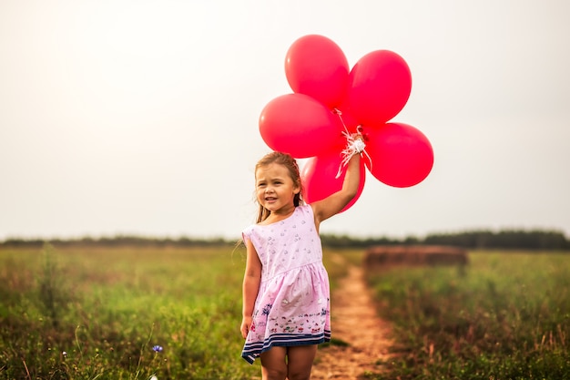 niña corre con globos rojos en el verano en la naturaleza