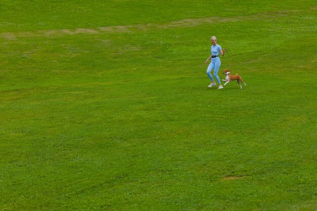 Niña corre con un perro en el parque en el césped al atardecer, pasea a una mascota en la naturaleza.