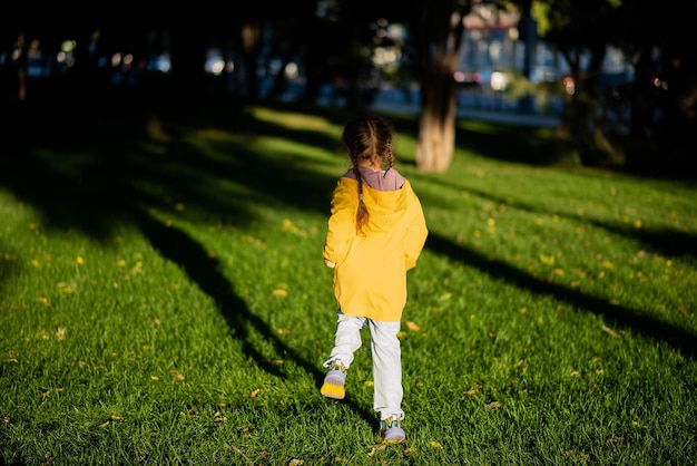 La niña corre sobre el césped verde bajo los rayos del atardecer.