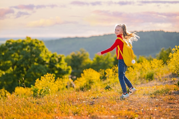 Niña corriendo por la noche con una mochila en la naturaleza en el fondo de un prado de flores, estepa, estilo de vida activo y saludable