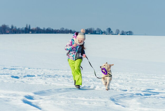 Niña corriendo con perro en la nieve