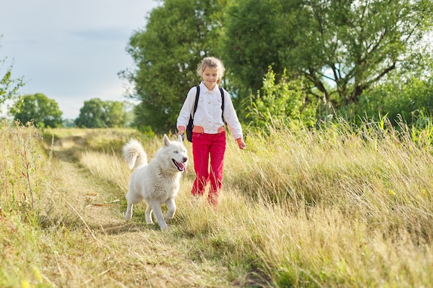 Niña corriendo con perro en la pradera. Niño jugando con mascota en la naturaleza, estilo de vida activo y saludable de los niños, amistad de animales y seres humanos