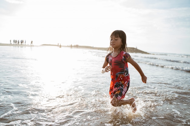 Niña corriendo en la playa mientras juega agua