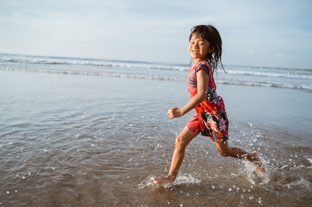 Niña corriendo en la playa mientras juega agua