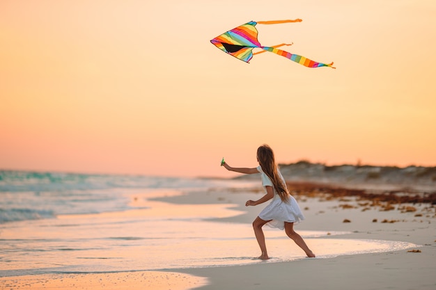 Niña corriendo con volar la cometa en la playa tropical. Niño juega en la orilla del océano.