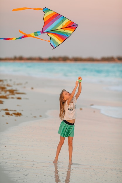 Niña corriendo con volar la cometa en la playa tropical. Niño juega en la orilla del océano.