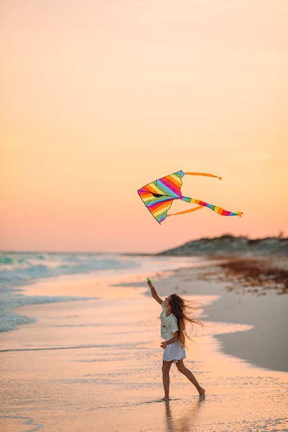 Niña corriendo con volar la cometa en la playa tropical. niño juega en la orilla del océano.