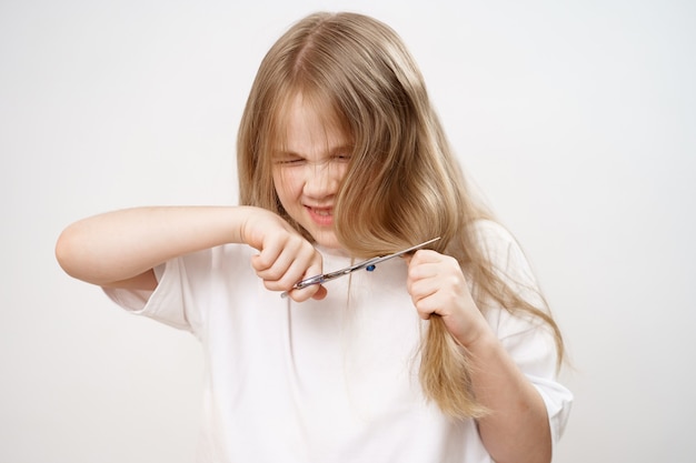 La niña corta su cabello largo con unas tijeras en blanco.