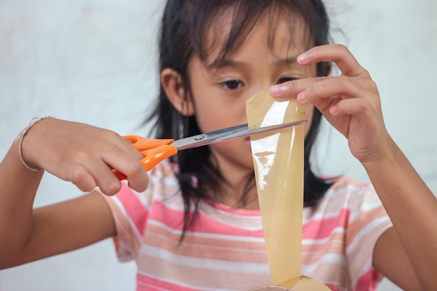 Una niña cortando un trozo de papel con unas tijeras.